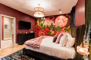 Une chambre à coucher comprenant un lit, un téléviseur, une décoration murale et une salle de bain avec douche et toilettes.