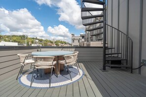 Une terrasse sur le toit avec une table ronde et des chaises, un escalier en colimaçon et une vue sur le paysage urbain.