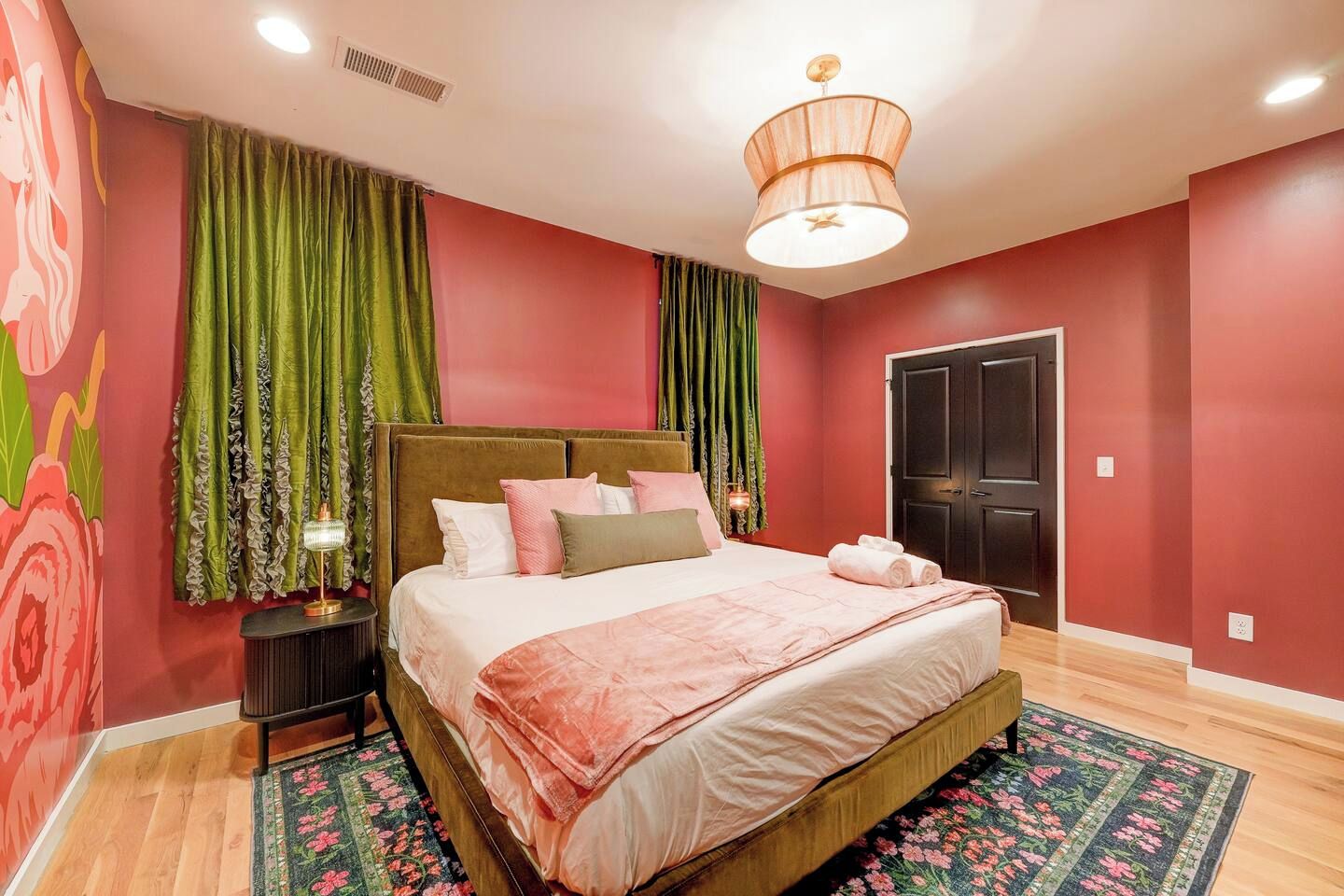 A bedroom with a bed, curtains, a nightstand, a lamp, a door, and a ceiling light fixture.