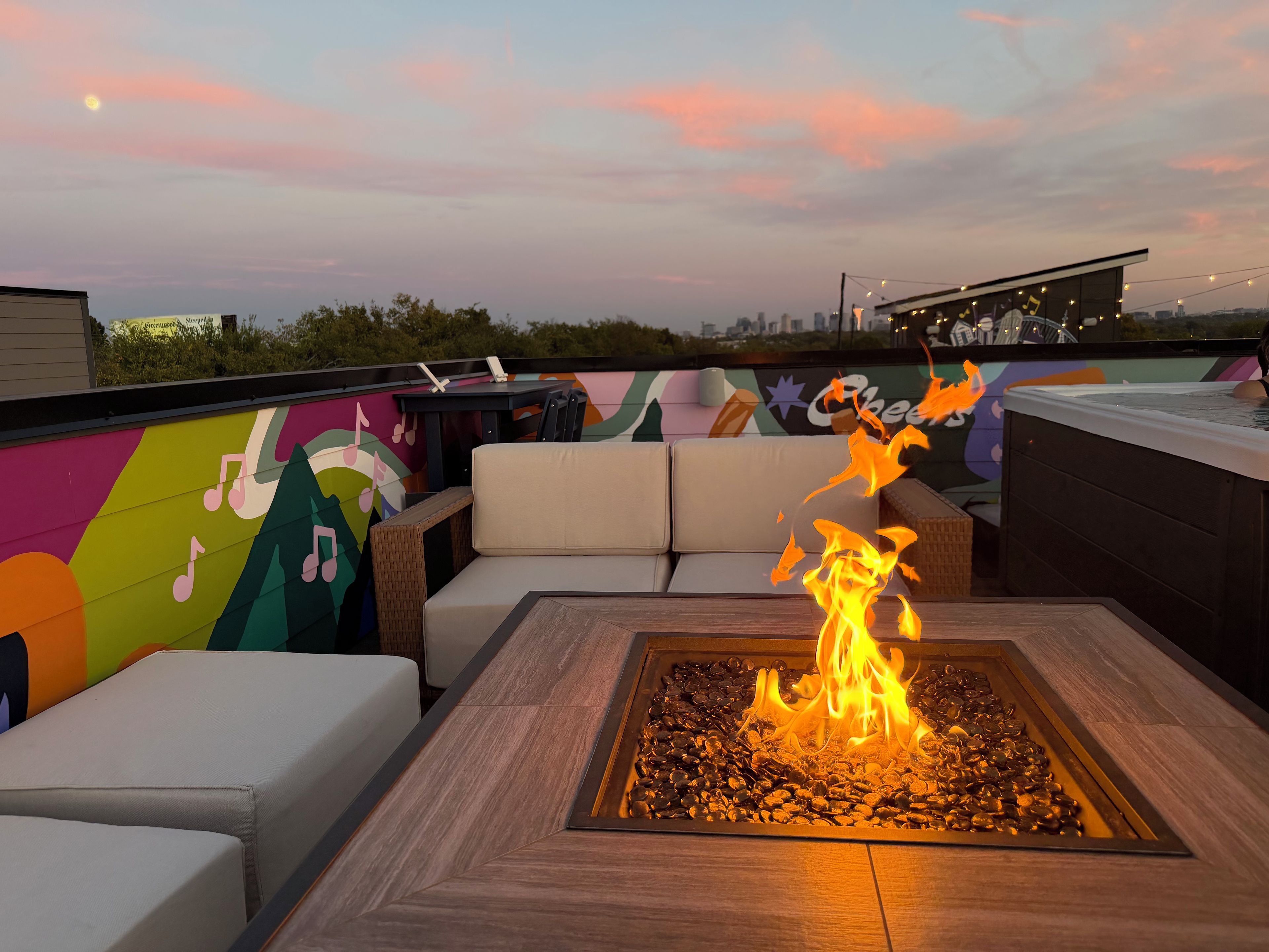 Eine Dachterrasse mit Feuerstelle, Sitzgelegenheiten und einem farbenfrohen Wandgemälde.
