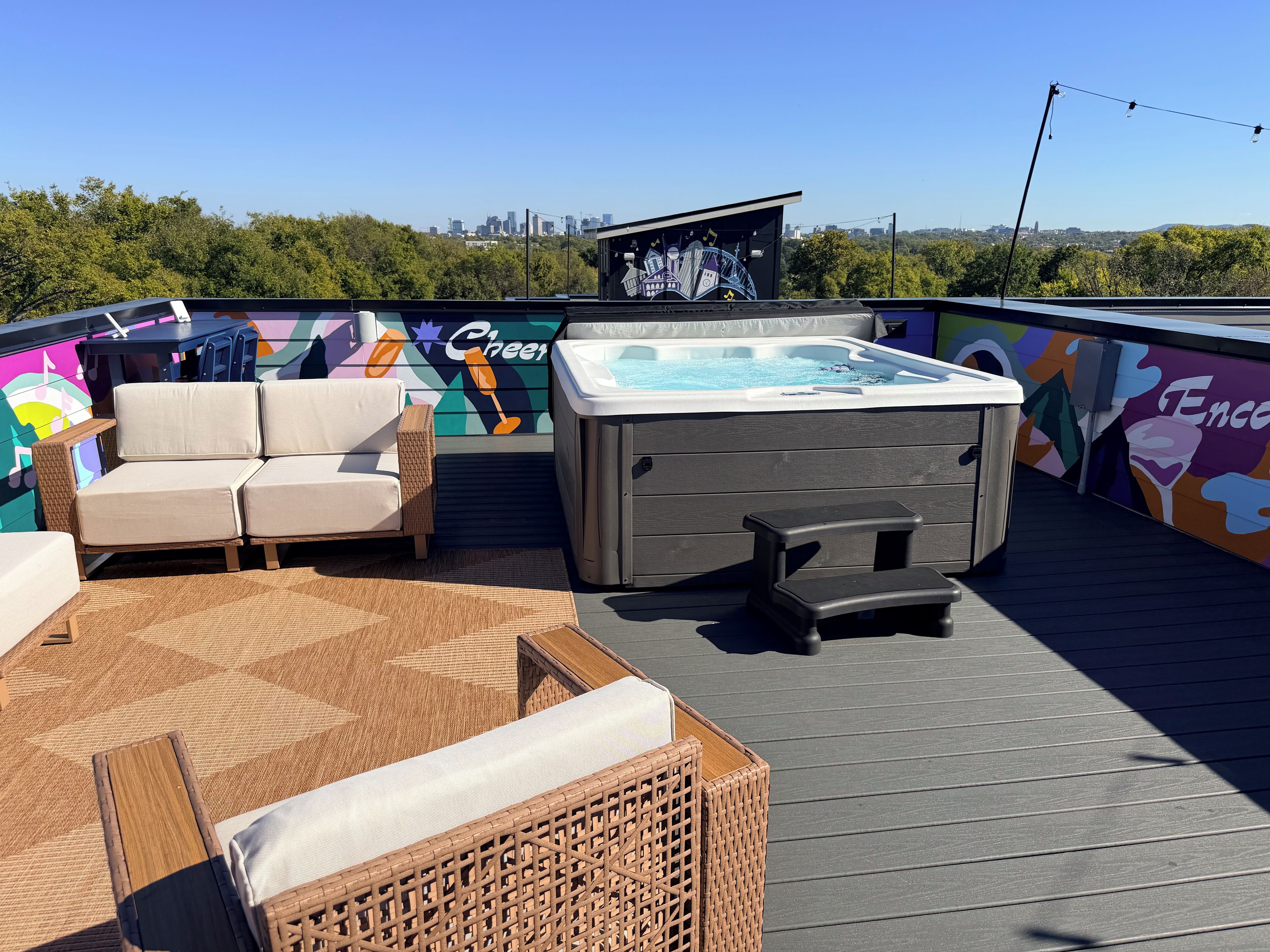 A rooftop deck with a hot tub, lounge chairs, and a mural.