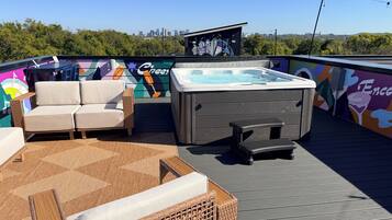 A rooftop deck with a hot tub, lounge chairs, and a mural.