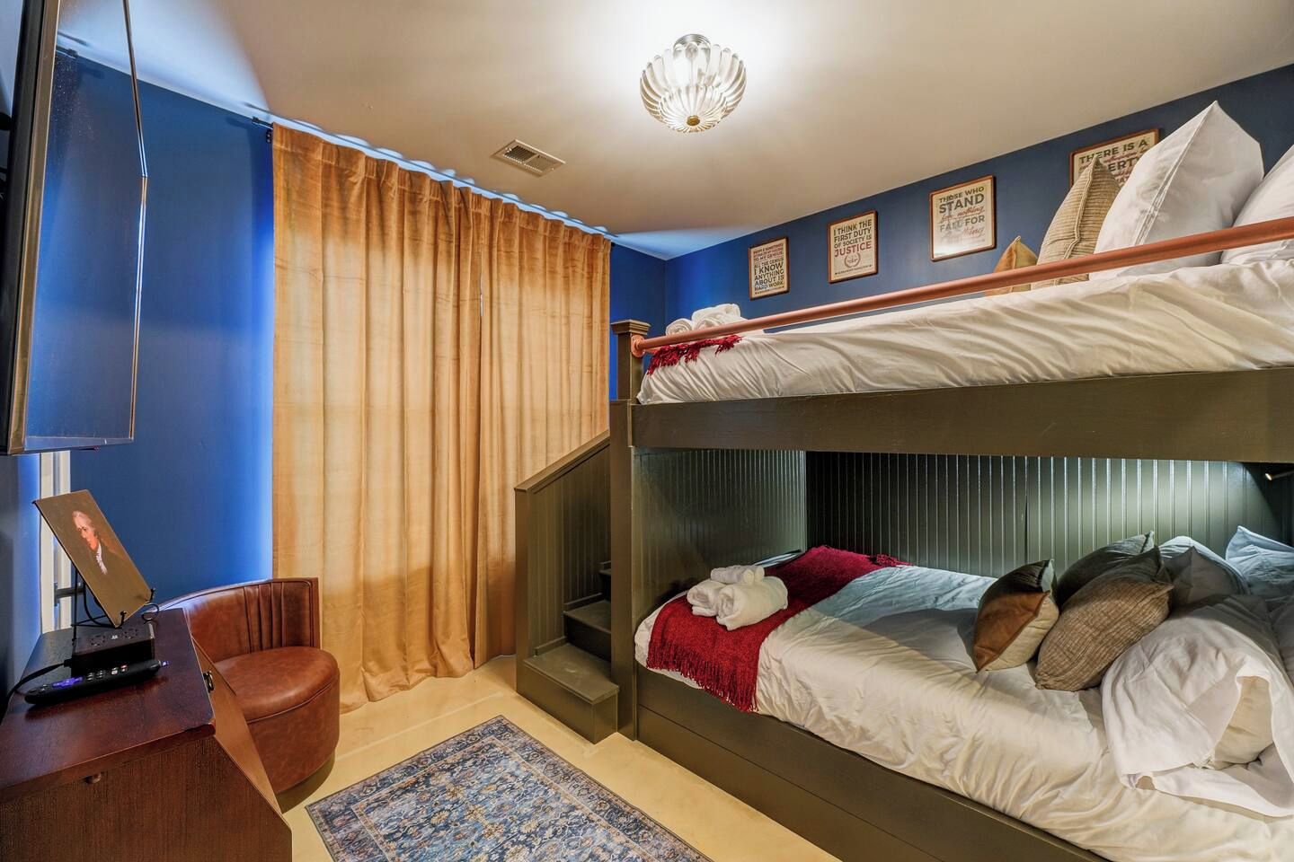 A bunk bed room with a desk, a chair, a patterned rug, and a curtain.