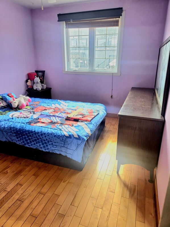 A bedroom with a bed, a dresser, a window, and a wall-mounted TV.