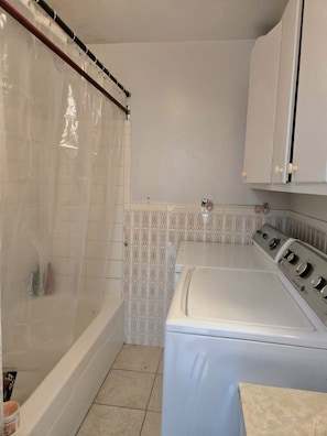 A laundry room with a washing machine, a bathtub with a shower curtain, and tiled walls.