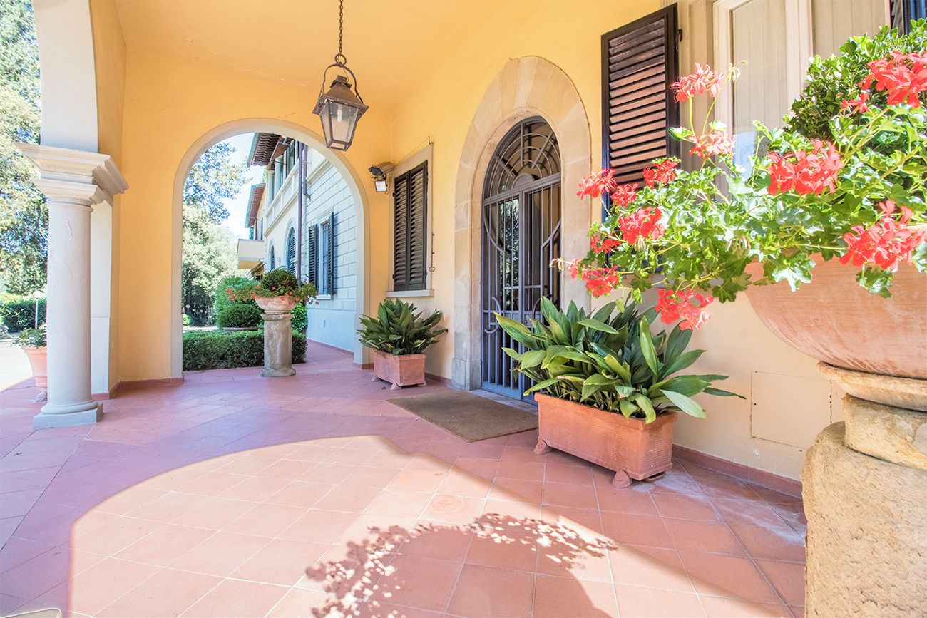 A covered outdoor area with a tiled floor, potted plants, and a large planter with flowers.