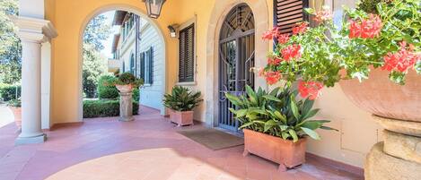 A covered outdoor area with a tiled floor, potted plants, and a large planter with flowers.