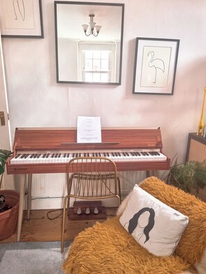 Un piano, una silla, un cojín mullido, un cuadro enmarcado y un espejo en la pared.