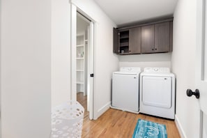 A laundry room with two white washing machines, a wooden cabinet above, and a white door with a black handle. - Charlotte Retreat - Hot Tub, Fire Pit & Uptown (Charlotte)