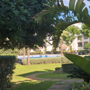 A well-maintained garden with a pathway, lush greenery, and a pool area in the background. - La Torre Escape - A Charming Two Bedroom Apartment at La Torre Golf Resort (Torre-Pacheco)