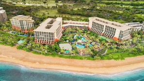 Ett semesterhotell vid stranden med flera hotellbyggnader, ett centralt poolområde och en strand.