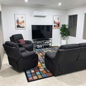 Ein Wohnzimmer mit einem Flachbildfernseher, zwei schwarzen Sofas, einem farbenfrohen Teppich und zwei gerahmten Bildern an der Wand.