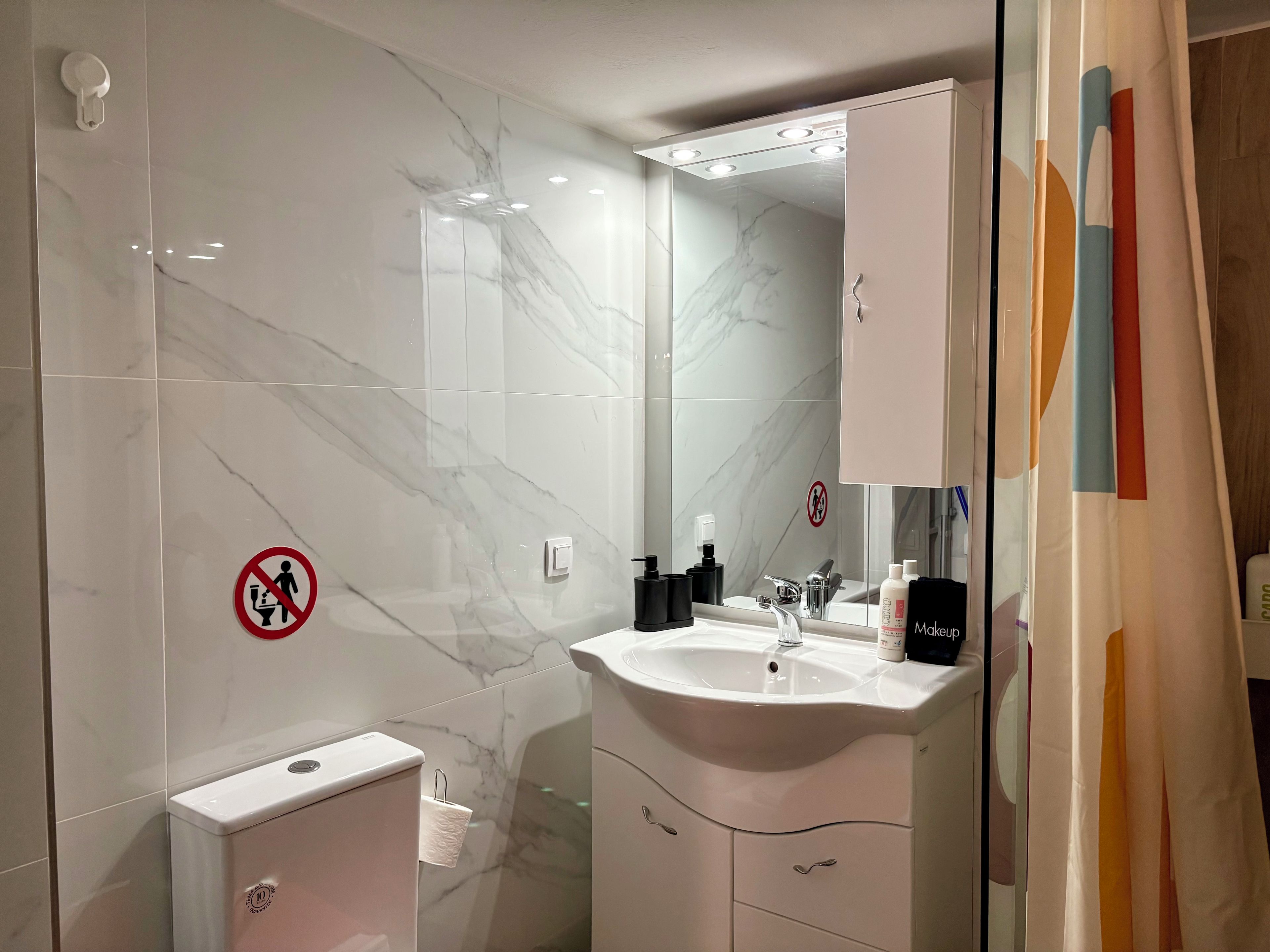 Une salle de bain avec un mur en marbre, un lavabo, des toilettes et une douche.