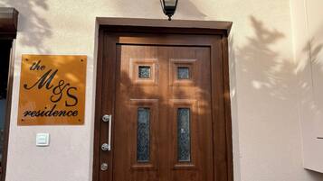 A wooden door with a metal handle and a glass panel, a wall-mounted light fixture above, and a sign reading 'the M&S residence' on the wall.