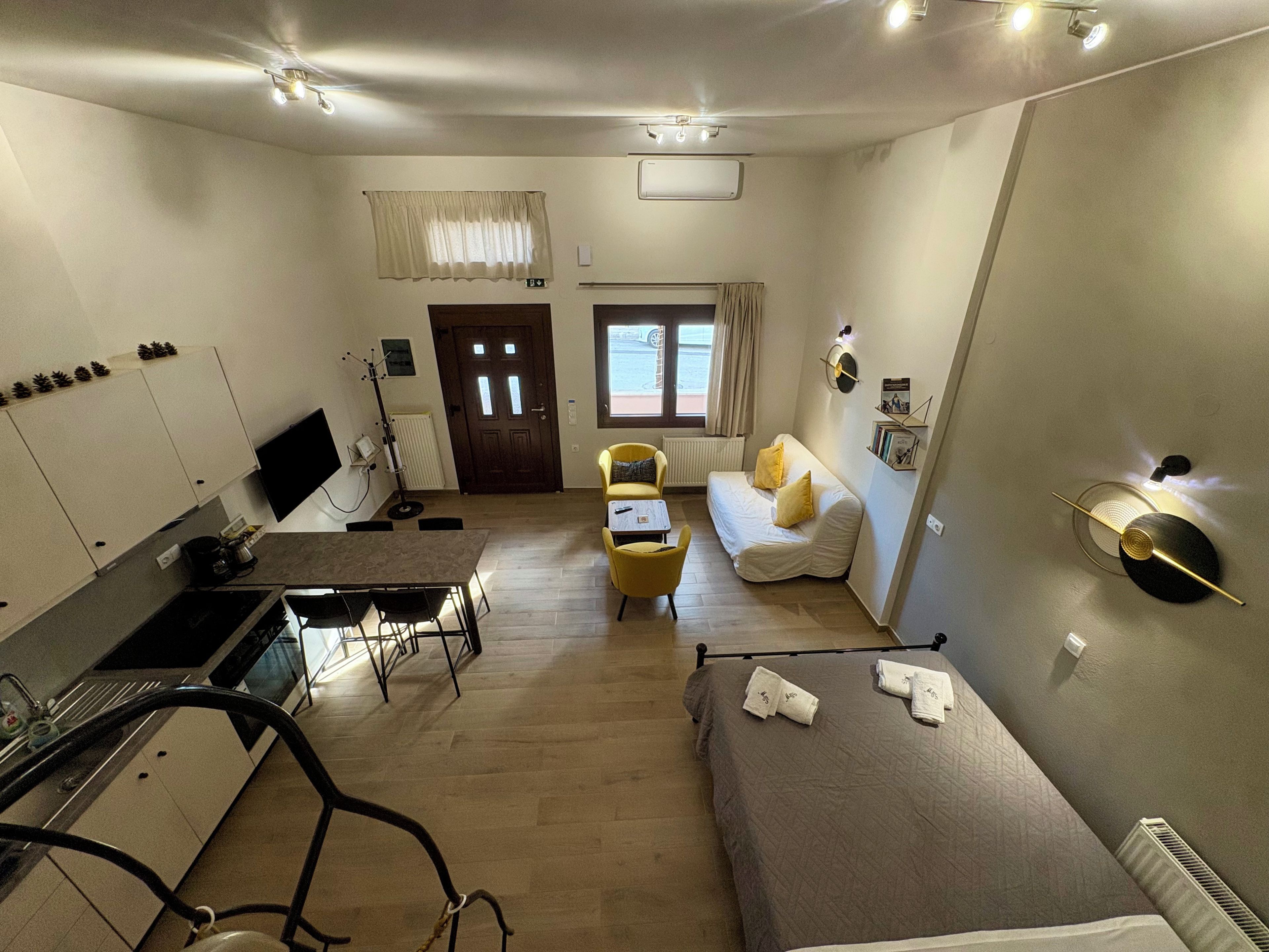 Habitación de hotel compacta con kitchenette, sofá, cama y ventana con cortinas.