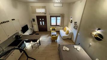 Habitación de hotel compacta con kitchenette, sofá, cama y ventana con cortinas.