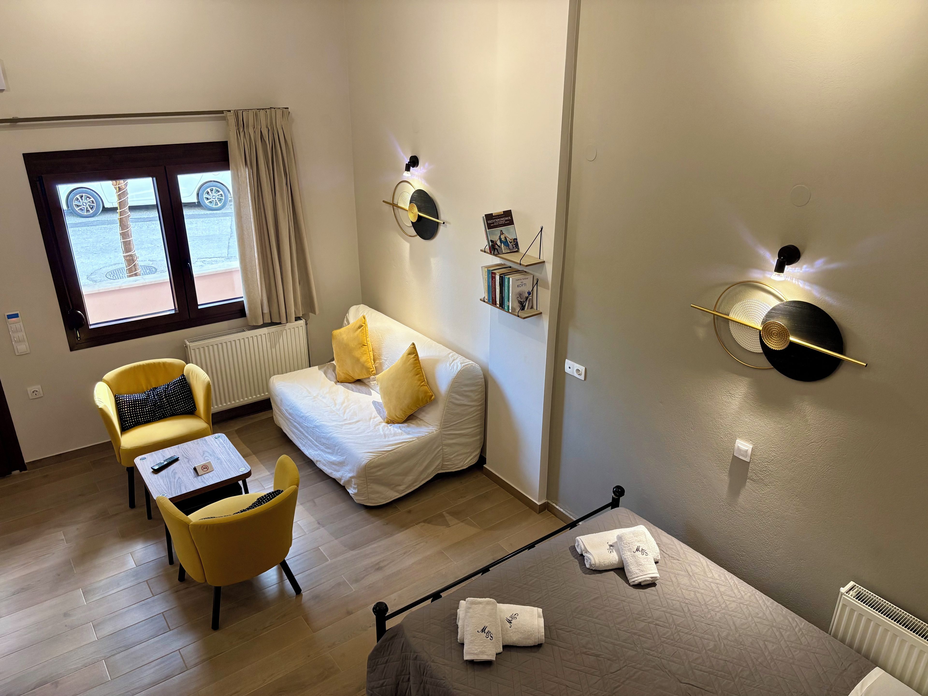 Hotellihuone, jossa on sänky, sohva, tuoli, pieni pöytä ja ikkunasta avautuva näkymä kadulle.