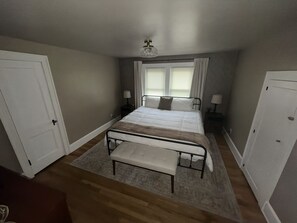 A bedroom with a bed, bedside tables, a bench, a ceiling fan, and a window with curtains. - Stay Awhile • King Bed • Pet Friendly • 2BR (Elyria)