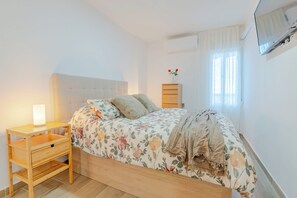 A bedroom with a bed, bedside table, lamp, and a wall-mounted TV. - New Listing (Benalmádena)
