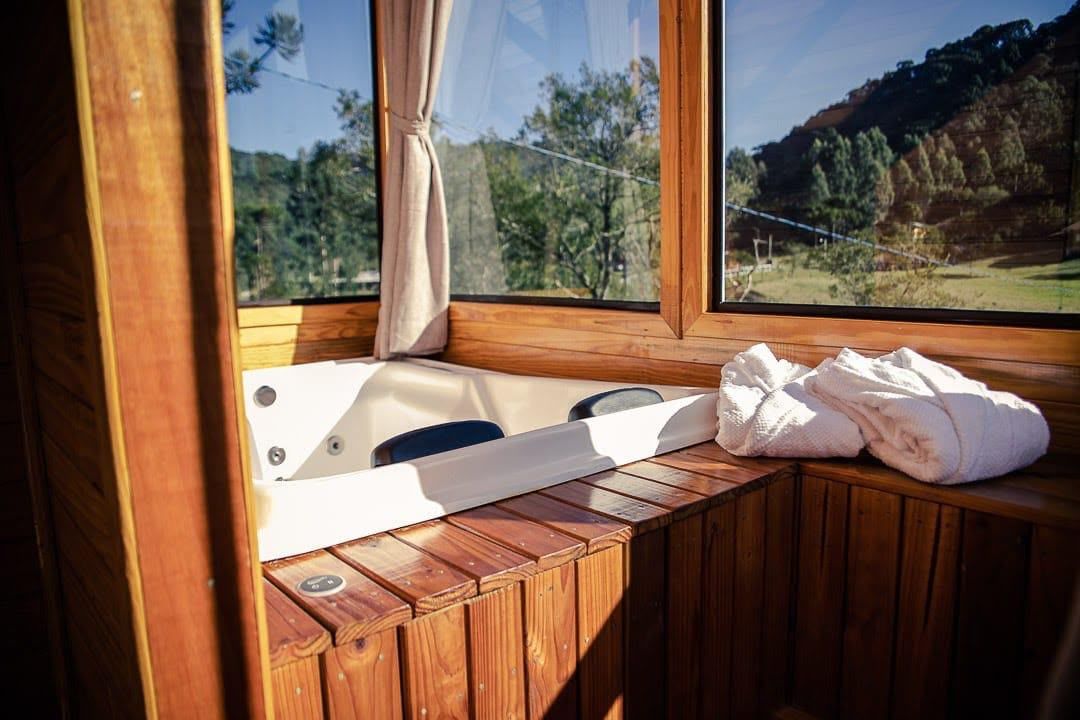 Una cabaña de madera con un banco de madera, una bañera y vistas de un paisaje boscoso a través de una ventana.