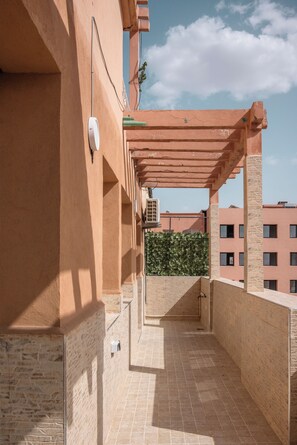A covered outdoor balcony with a tiled floor, a green hedge, and a building in the background. - Marrakech 2 Bedroom 2 Bathroom Luxury Apartment,Large Balconies and Free Parking (Marrakech)