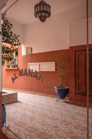 Une façade d’immeuble avec une enseigne indiquant « AL MANAR » et un pot de fleurs posé sur le sol.