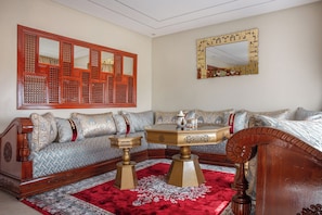 Une pièce au décor traditionnel, comprenant un canapé, une table basse, un miroir décoratif et un tapis à motifs.