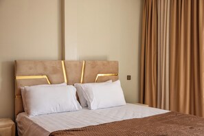Une chambre d’hôtel avec un lit, deux oreillers, une tête de lit ornée de motifs dorés et un rideau.