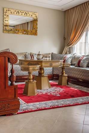 A room with a round wooden coffee table with ornate legs, a sofa with patterned cushions, and a red and white patterned rug. - Marrakech 2 Bedroom 2 Bathroom Luxury Apartment,Large Balconies and Free Parking (Marrakech)