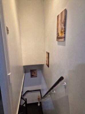 A narrow stairway with a handrail, a small vase with dried plants, and two framed pictures on the wall. - Welcome to Your Stylish East London Getaway!
Newly renovated from top to bottom (Barking)