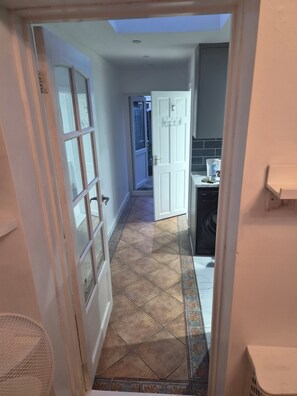 Un pasillo con piso de baldosas, una puerta con manija y un ventanal con vistas al exterior.