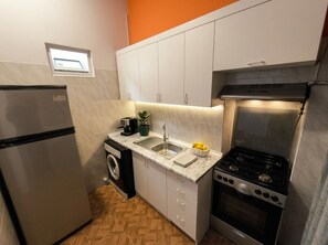 Cozinha compacta com geladeira, máquina de lavar, pia, fogão e armários.