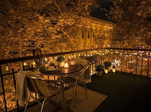 An outdoor dining area with a table and chairs, surrounded by a railing with string lights. - Heart of Baku: Targovi Apartment with Stunning Boulevard View (Baku)