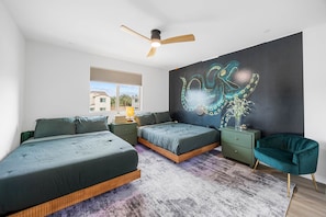 A modern bedroom with two beds, a ceiling fan, a large wall mural, and a view of the outside. - Design Estate w/Heated Zero-Edge Pool & Game Room (Coachella)