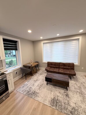 A modern living room with a sofa, coffee table, and a dining area with a table and chairs. - 1.2 Miles to NIH & Walter Reed - Walk to Metro (Bethesda)