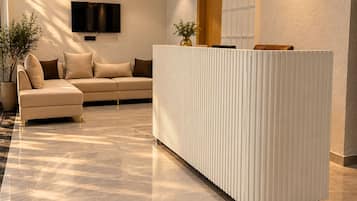 A modern reception area with a marble floor, a sofa, a TV, and a decorative light fixture.