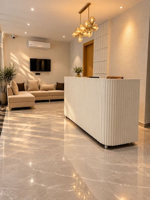 Un área de recepción moderna con suelo de mármol, un sofá, un televisor y una lámpara decorativa.