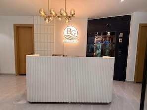 A reception desk with a logo, a modern chandelier, and an elevator in the background. - Bless Ganga by Solvaya Rishikesh (Rishikesh)