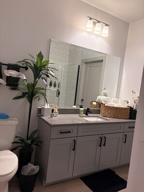 Ein modernes Badezimmer mit einem weißen Waschbecken, einem großen Spiegel und einer Topfpflanze.