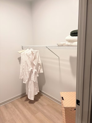 Un coin de pièce avec un plancher en bois, un porte-serviettes blanc sur lequel sont pliées des serviettes, et un peignoir blanc accroché à un crochet.