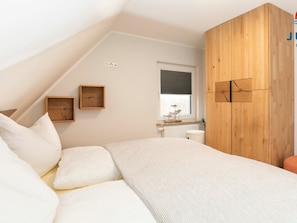 Ein Schlafzimmer mit geneigter Decke, einem Bett mit weißer Bettwäsche, einem Holzschrank und zwei an der Wand befestigten Bilderrahmen.