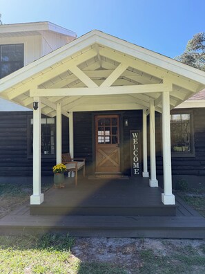 A wooden cabin with a porch, a welcome sign, and a bench. - The Cozy Cabin- 2 large bedrooms surrounded by views of old Florida (Williston)