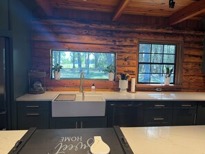 A kitchen with a wooden cabin-style interior, a large window with a view of trees, and a countertop with a dish soap bottle. - The Cozy Cabin- 2 large bedrooms surrounded by views of old Florida (Williston)