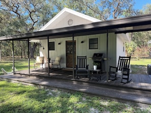A covered porch with outdoor seating, a grill, and a house in the background. - The Cozy Cabin- 2 large bedrooms surrounded by views of old Florida (Williston)