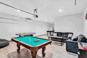A room with a pool table, a sofa, and a small table with a projector. - Coachella White House | Saltwater Pool, Spa & Games (Coachella)