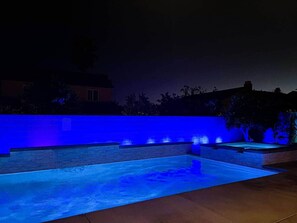 A swimming pool with a blue-lit wall and a clear night sky. - Coachella White House | Saltwater Pool, Spa & Games (Coachella)