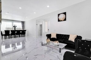 Un salon moderne avec un canapé noir, une table basse en verre et un coin repas comprenant une table et des chaises noires.