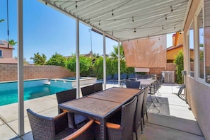 An outdoor patio with a pool, covered seating area, and a table. - Coachella White House | Saltwater Pool, Spa & Games (Coachella)