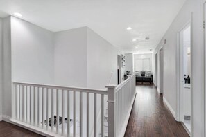 Un couloir avec une rambarde blanche, un banc et une porte au fond.