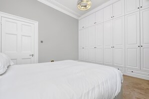 Quarto com cama grande, guarda-roupa branco e lustre.